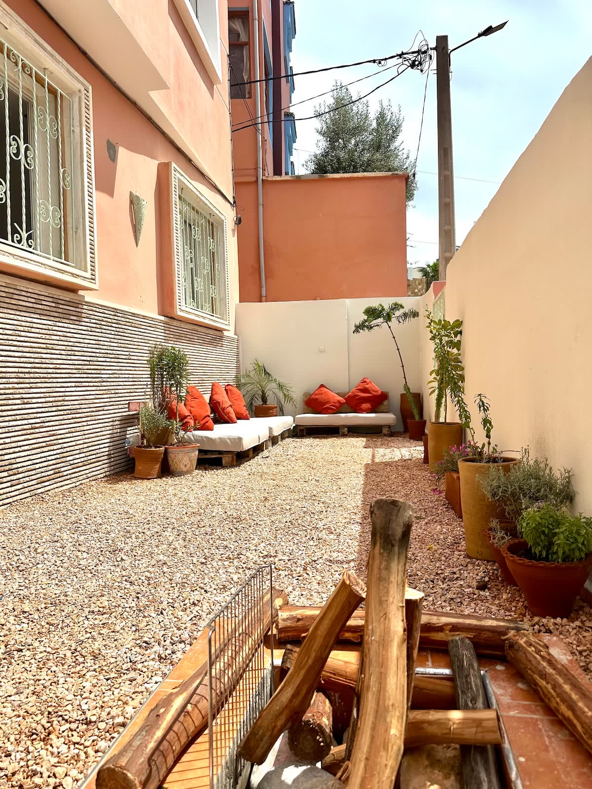 Gravel courtyard with red cushioned benches, potted plants and a stack of firewood