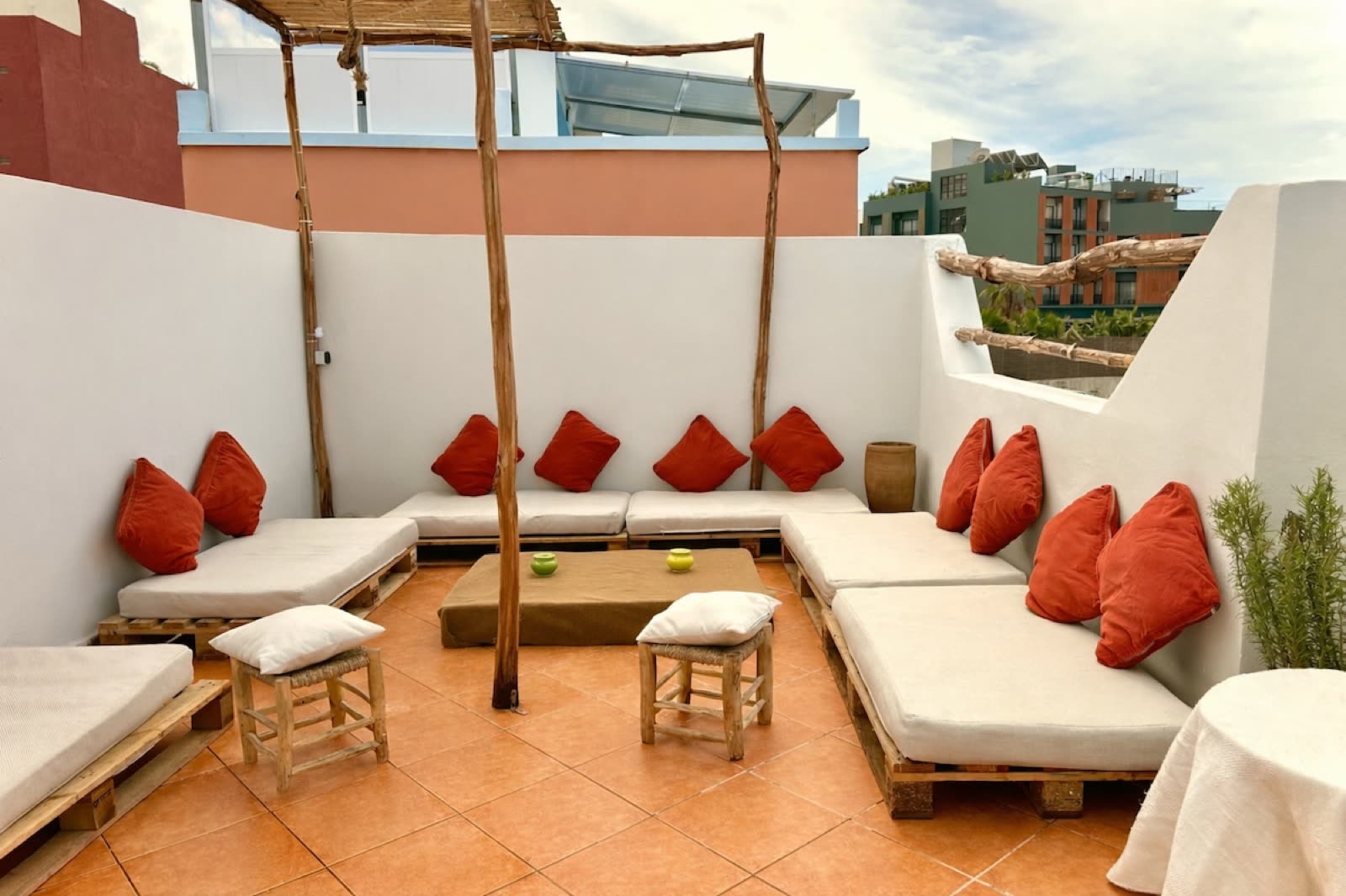 Rooftop terrace with white cushioned banquettes, red pillows and a wooden pergola
