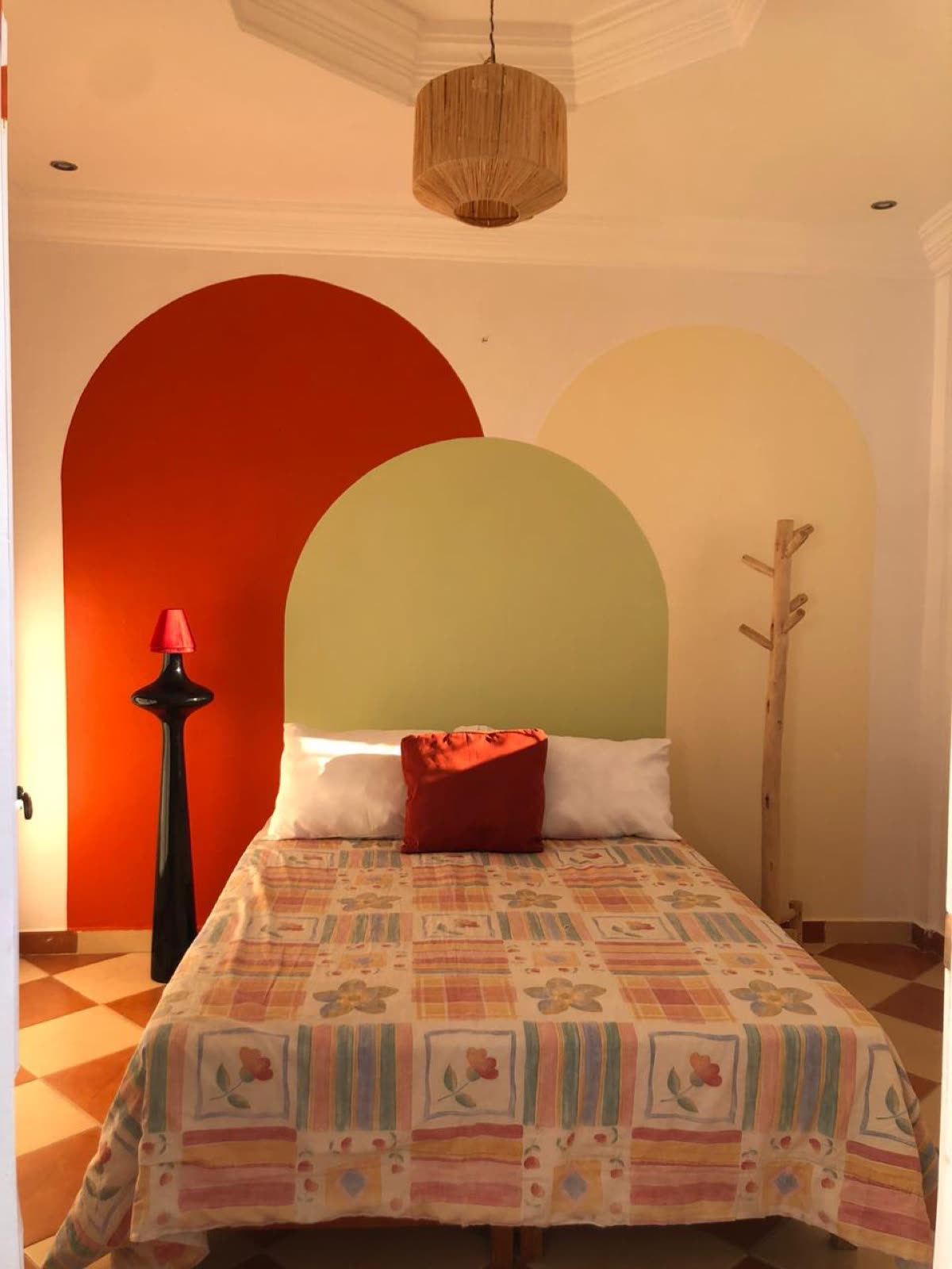 Bedroom with a hand-painted red and olive arch behind a double bed, checkered tile floor