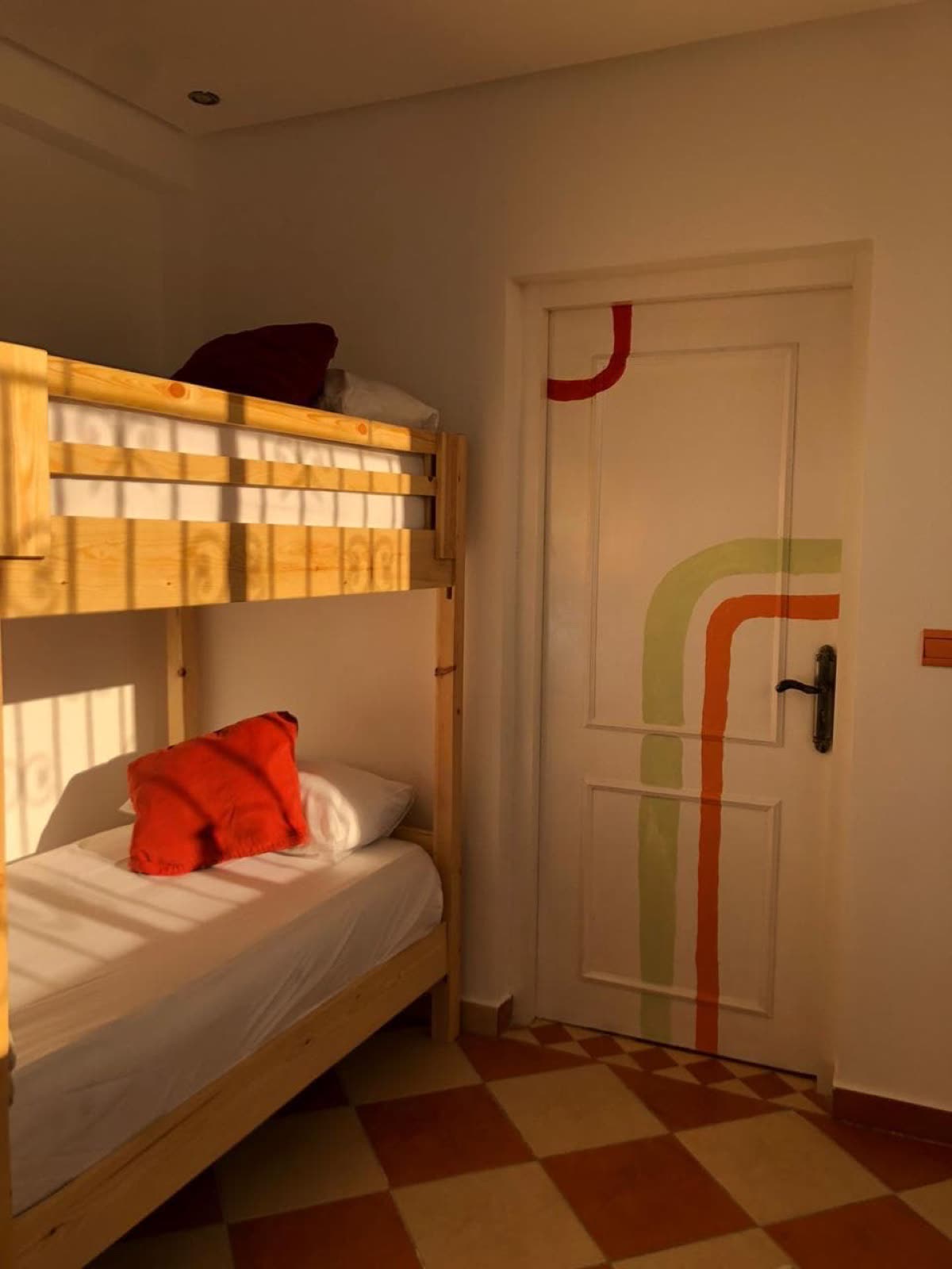 Handcrafted wooden bunk beds beside a painted door with a rainbow arc