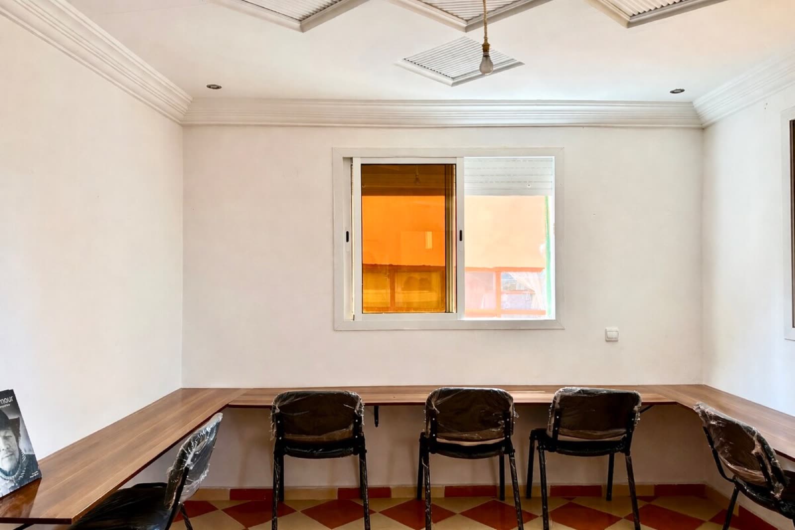 A long wooden work table running along a wall with chairs and a window above